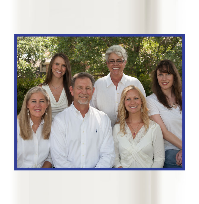 Group photo of six smiling adults outdoors, dressed in white.