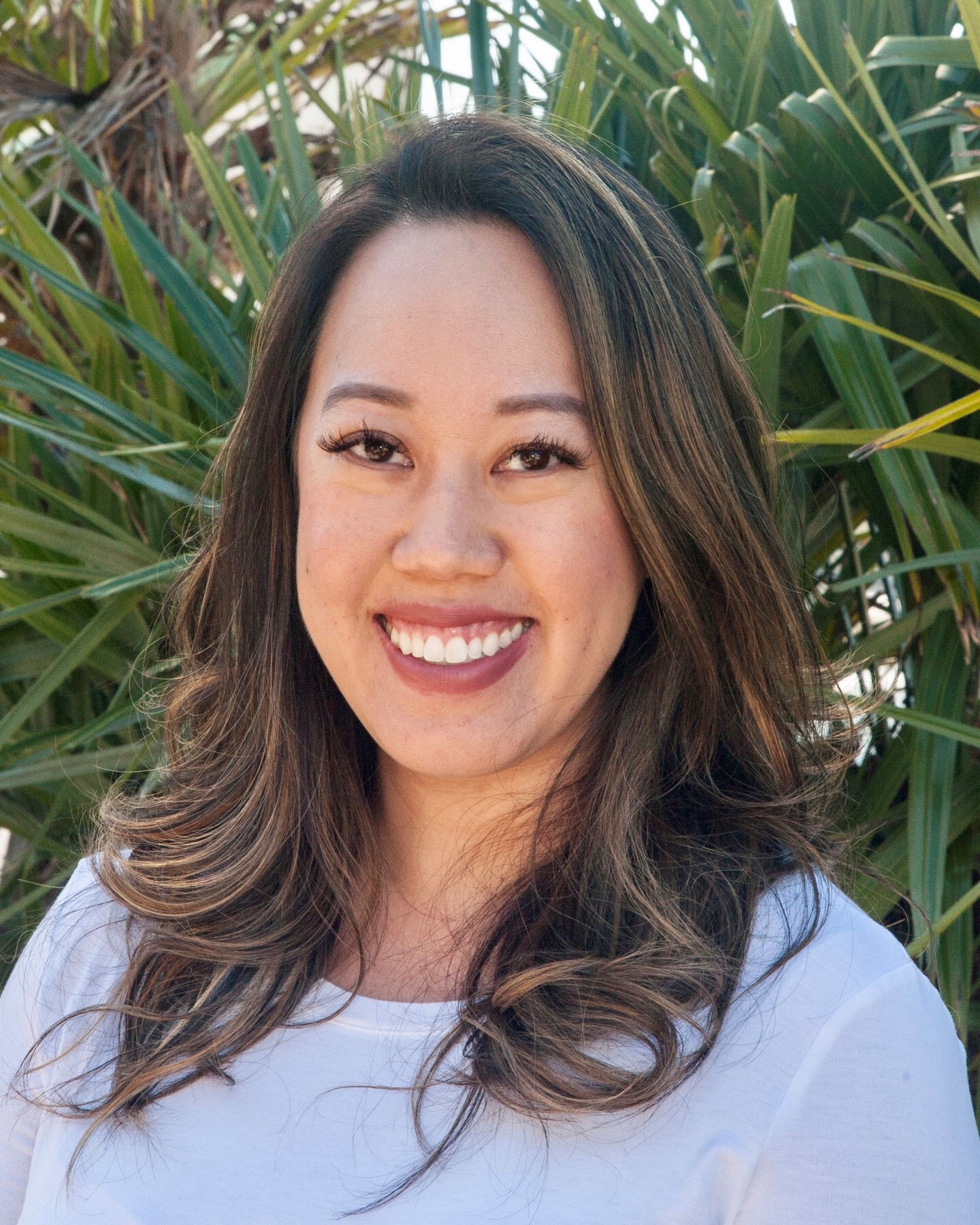 Smiling blonde woman outdoors with greenery in the background.